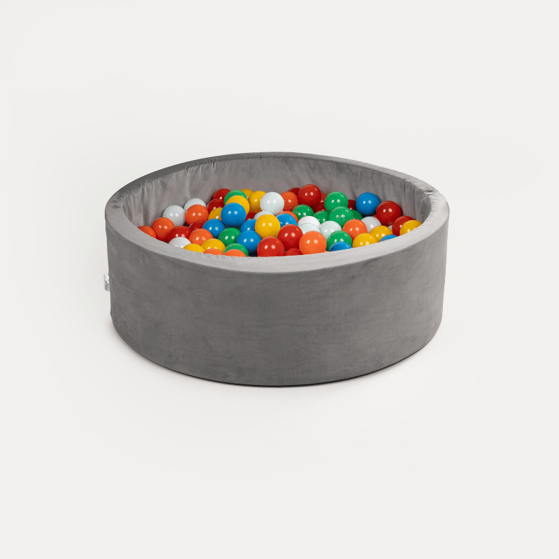Balle filtrante piscine en forme de bassin rond gris rempli de boules colorées dans un décor blanc.