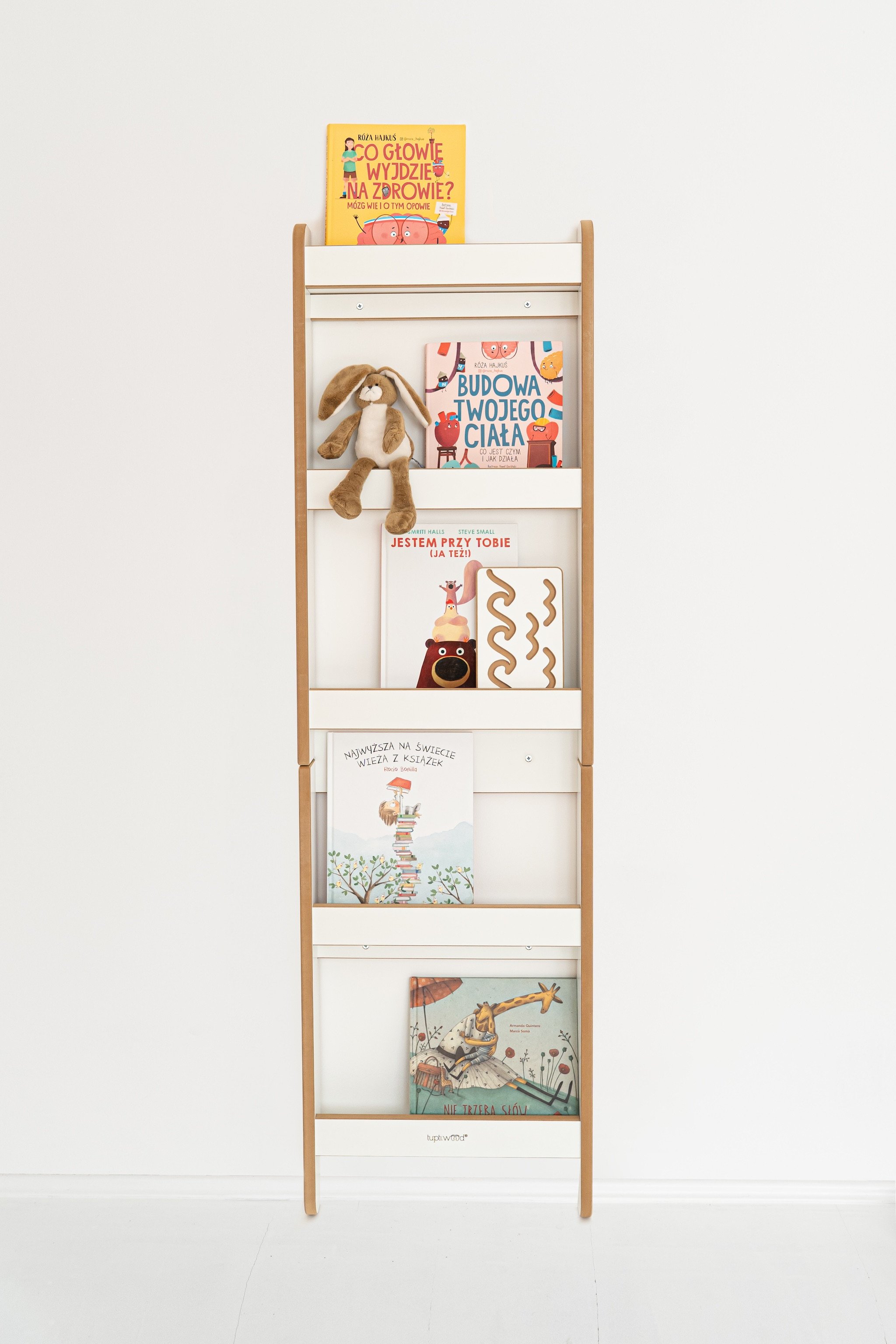 Étagère blanche à quatre niveaux avec livres et peluche, décor minimaliste dans un mur clair, jouets Montessori visibles.