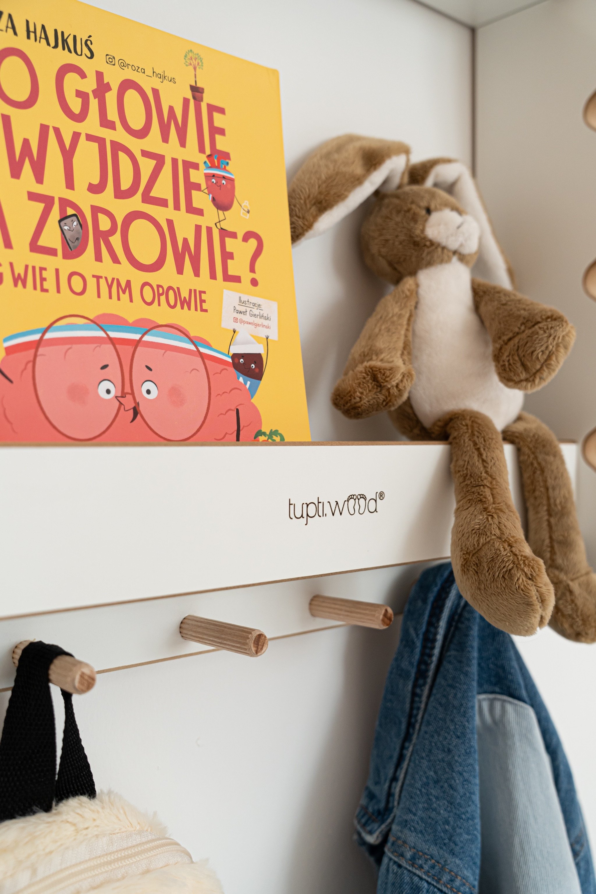 Livre jaune sur la santé de l’enfant et peluche marron accrochée dans un meuble, portant le texte “À quel âge…”.